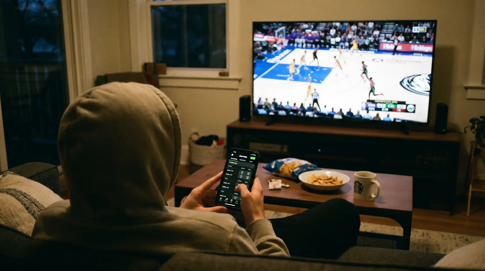 Apostador analizando líneas de hándicap en su móvil durante un partido de baloncesto